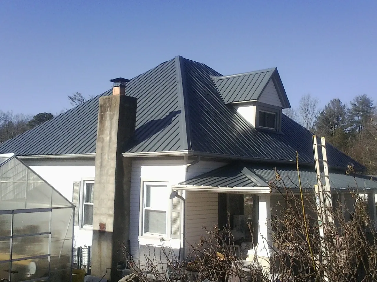 Dark blue standing seam metal roof on a white farmhouse with dormer — Slate & Tile Roof Repair by Roofing Brothers in Thomasboro