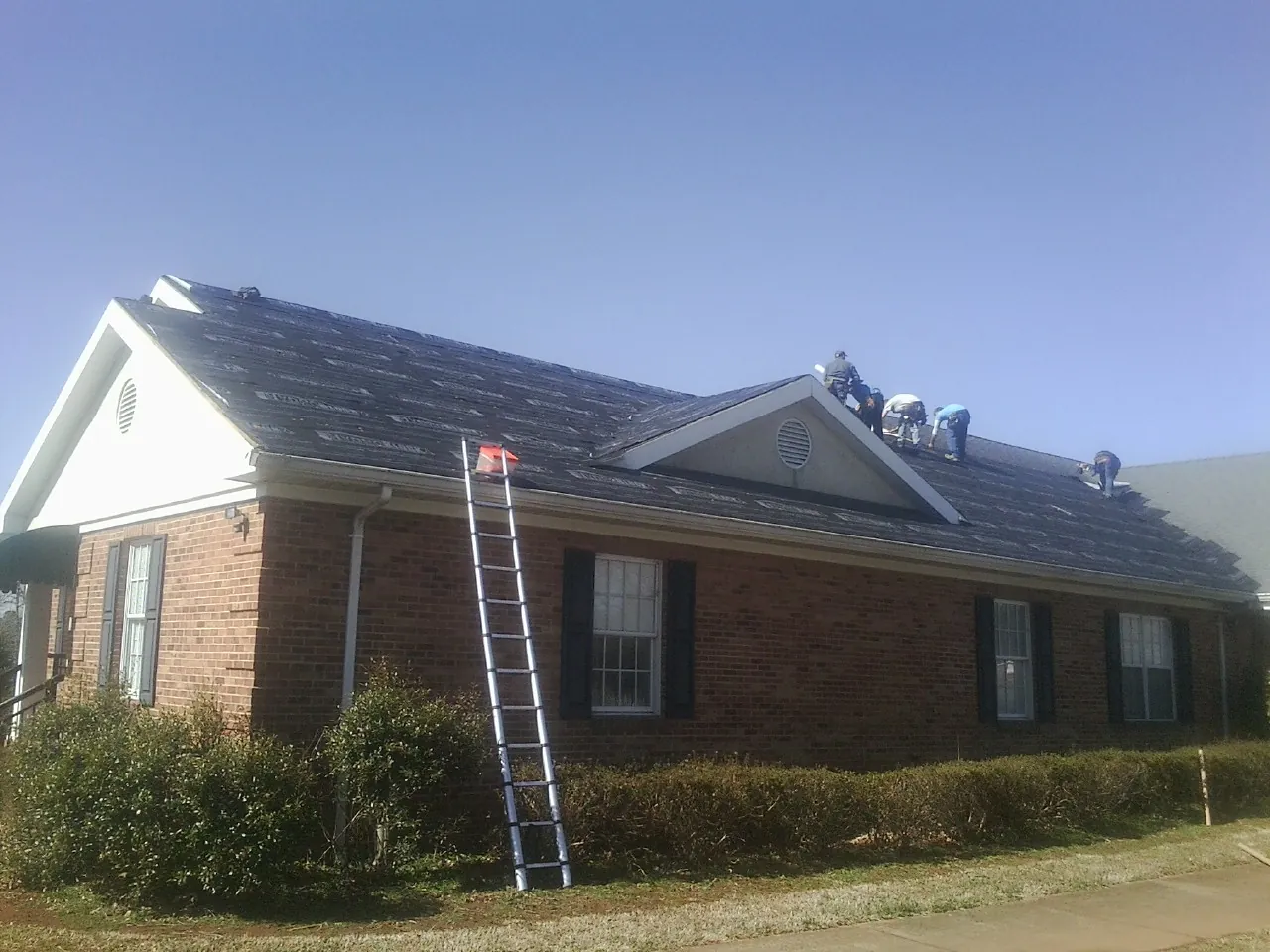 Crew tearing shingles off a brick ranch roof with a ladder set — Emergency Roof Repair work by our crew in Thomasboro