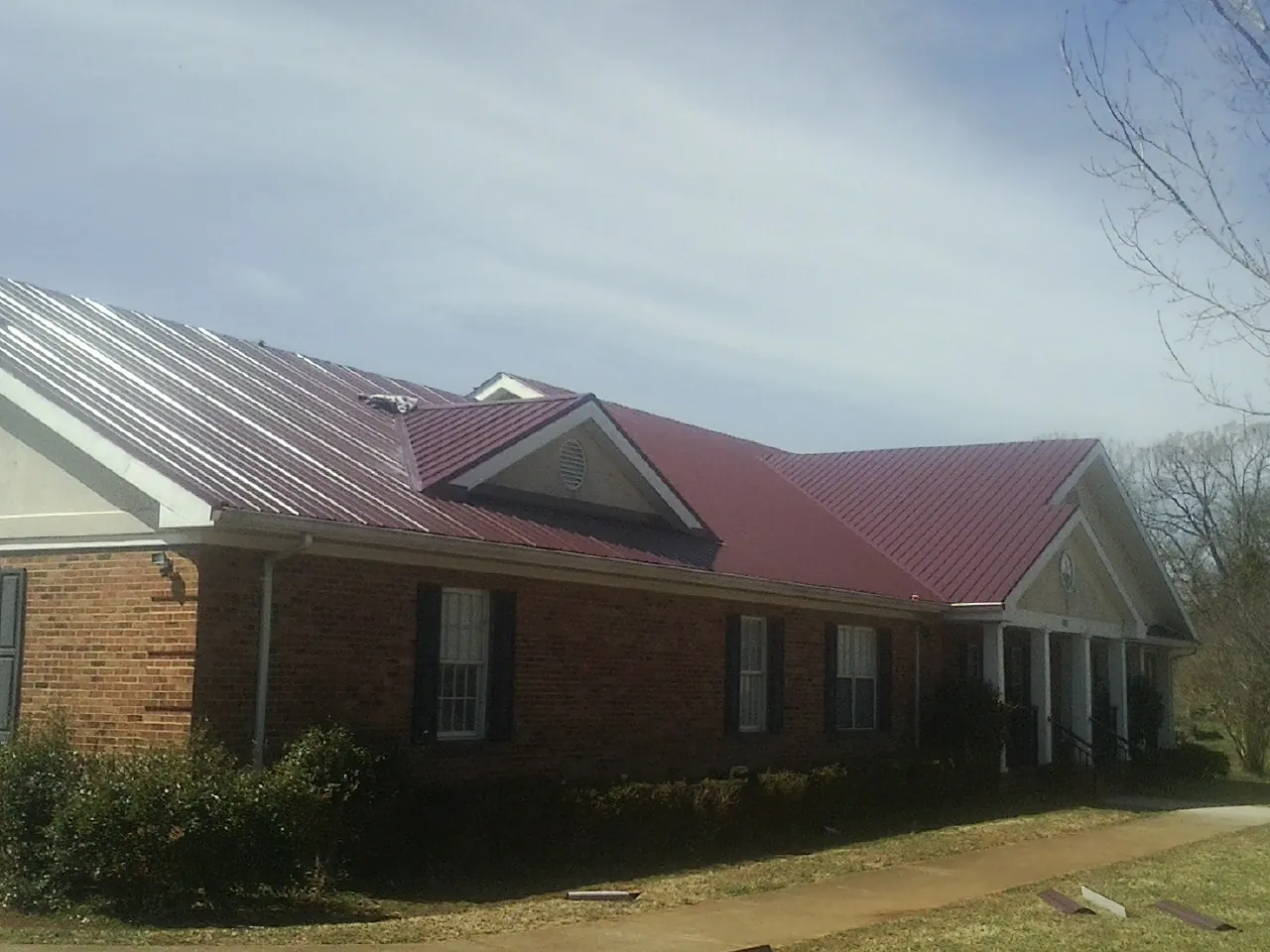 Red metal roof with gabled entries on a long brick building, from a Hail Damage Roof Repair job in Thomasboro