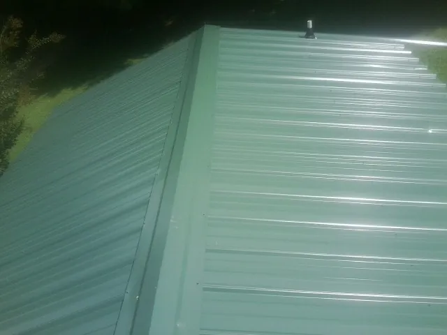 New green metal panels meeting at the ridge of a roof — Flat Roof Repair work by our crew in Thomasboro