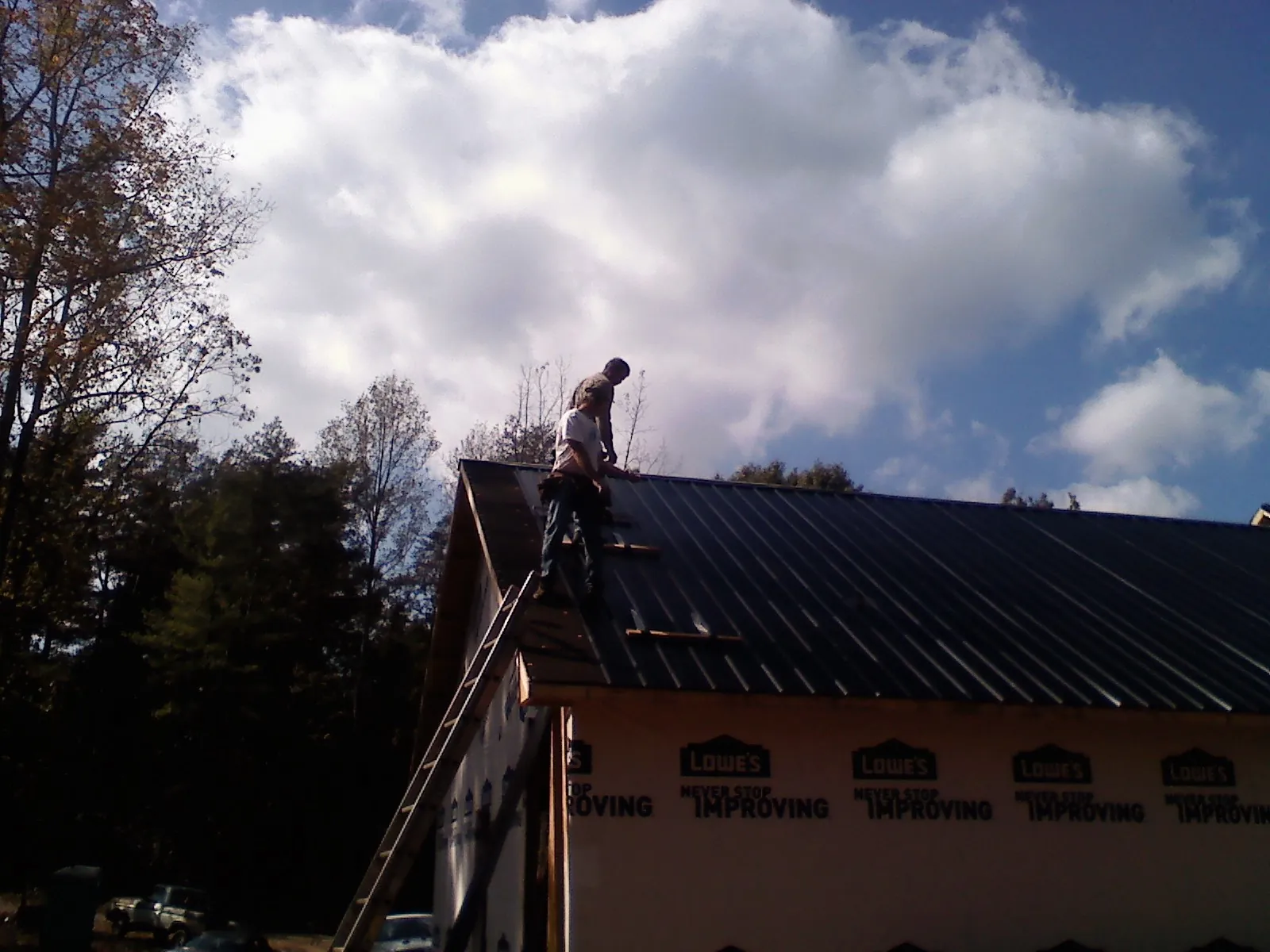 Roofer fastening dark metal panels high against a cloudy sky, from a Roof Inspection job in Thomasboro