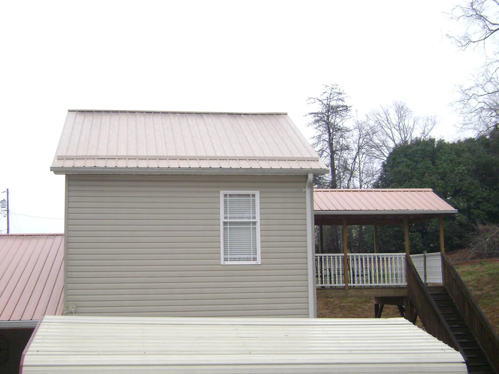 Tan metal roofs on a two story addition and attached porch, from a Roof Replacement job in Thomasboro